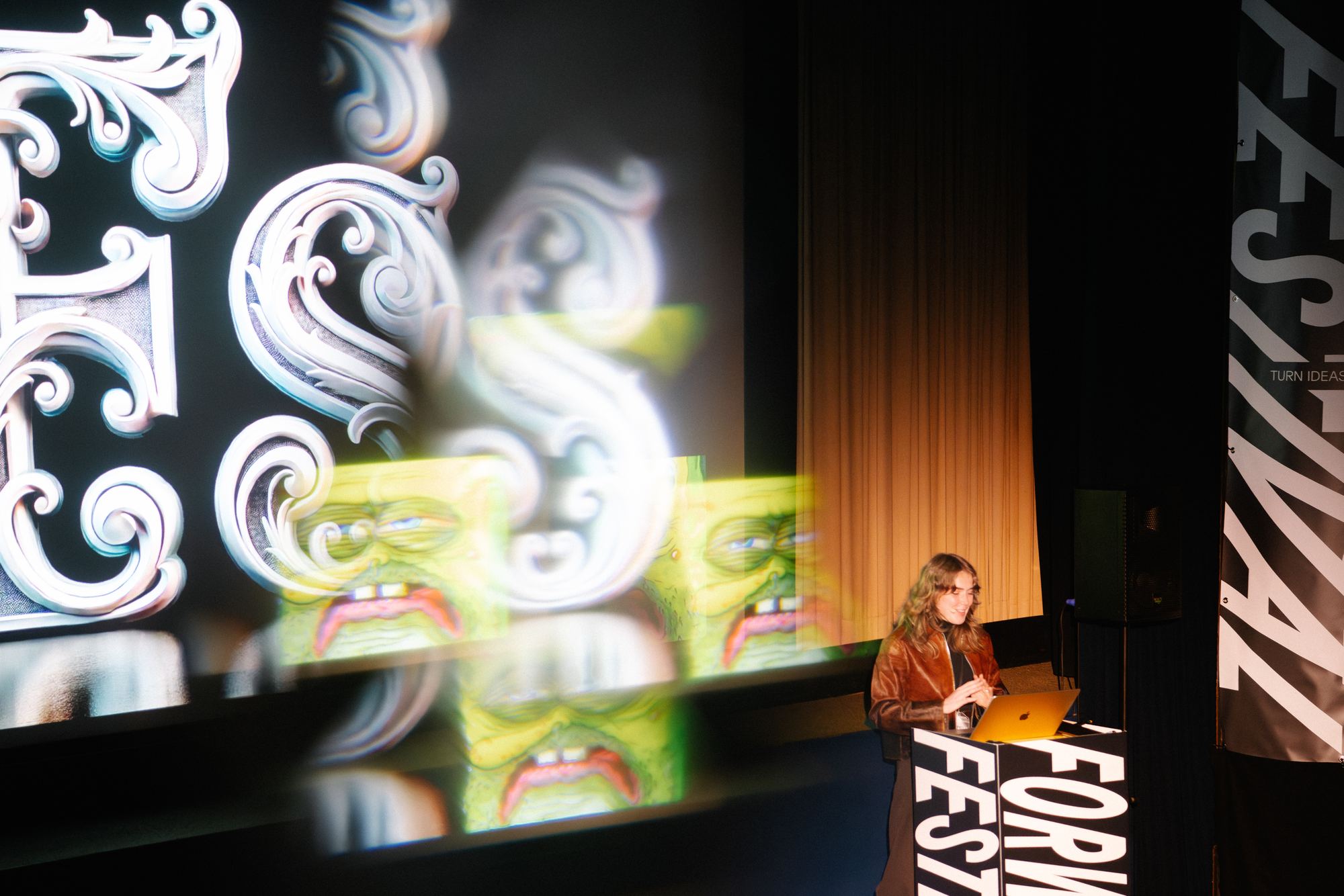 A speaker at the lectern beside a projection of ornate silver lettering.