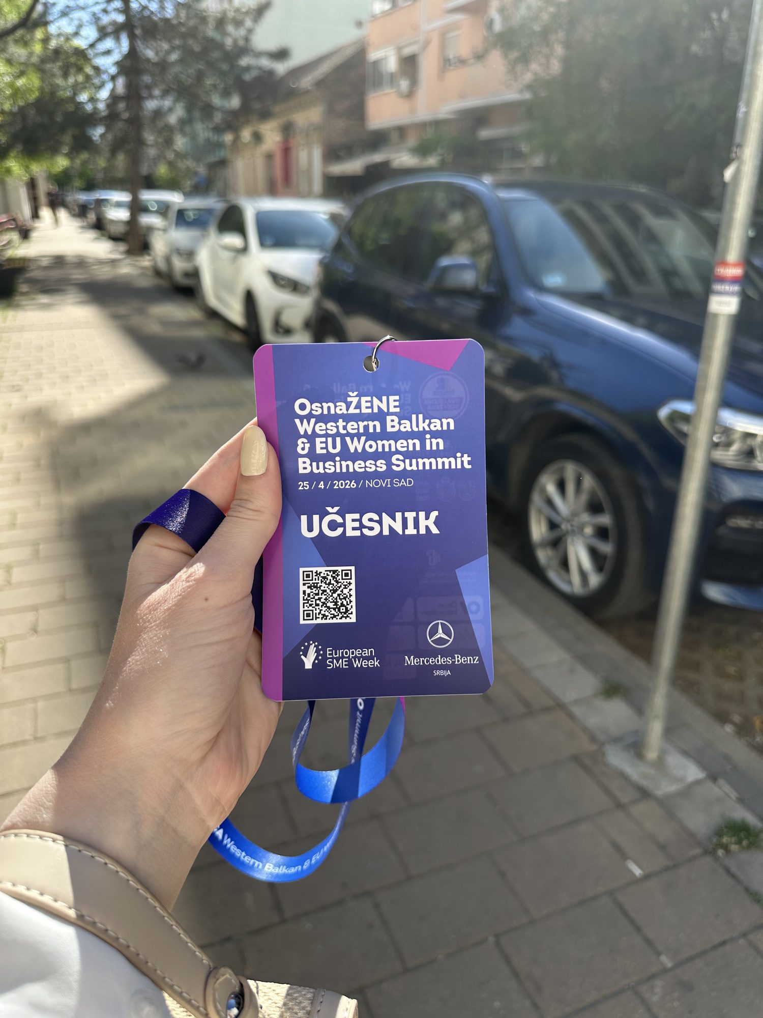 The summit badge held up on the street outside the venue, blue lanyard hanging loose against a row of parked cars.