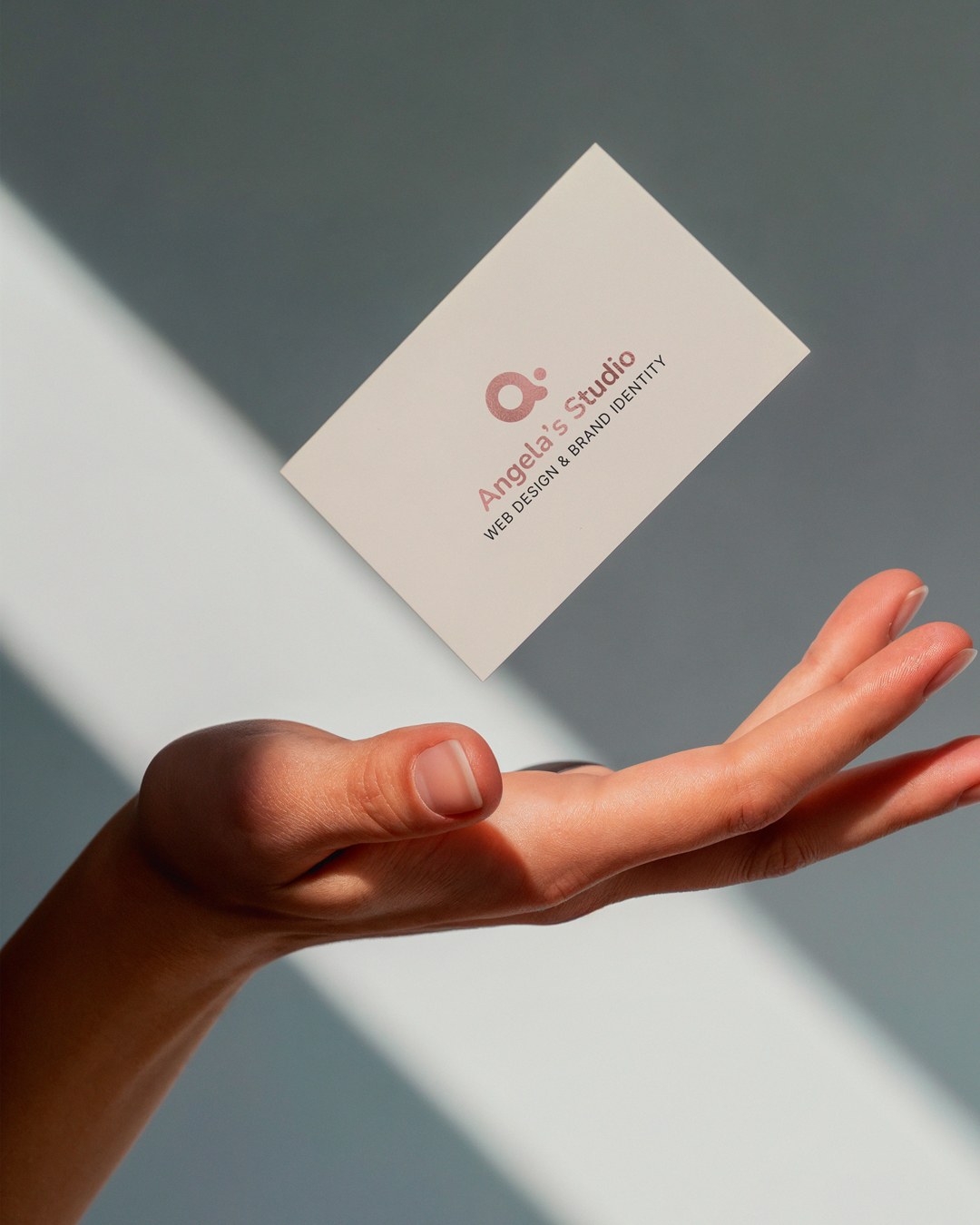 The business card, logo side, floating above an open hand in a slant of window light.